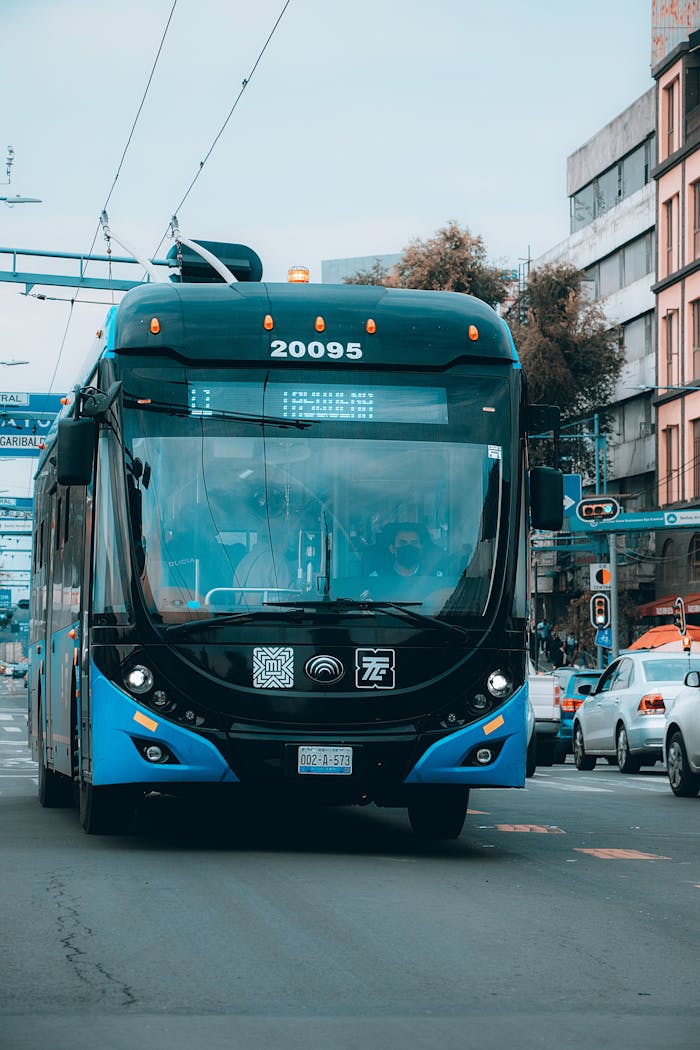 Blue public bus traveling on a busy urban street with cars and buildings visible.